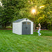 Woman walking towards a Lifetime 8x10 Shed in a lush garden at sunset, highlighting the shed's exterior and setting.