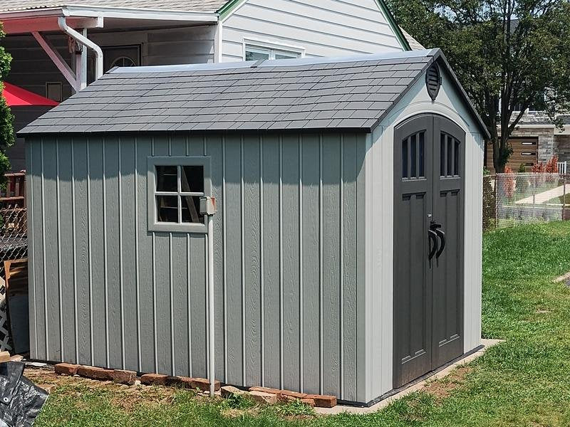Lifetime 8x10 ft. storage shed installed on a concrete pad, front angle view with closed double doors.