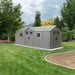 Gray Lifetime 20x8 outdoor storage shed with double doors, multiple windows, and a sloped roof, situated on a green lawn with trees and landscaping in the background.