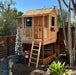 Little Cedar Playhouse 6x6 with holiday decorations in a backyard setting with rock garden