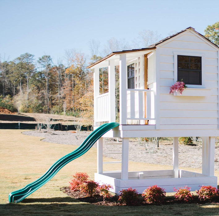 White-painted Little Cedar Playhouse 6x6 with green wave slide in an open autumn field