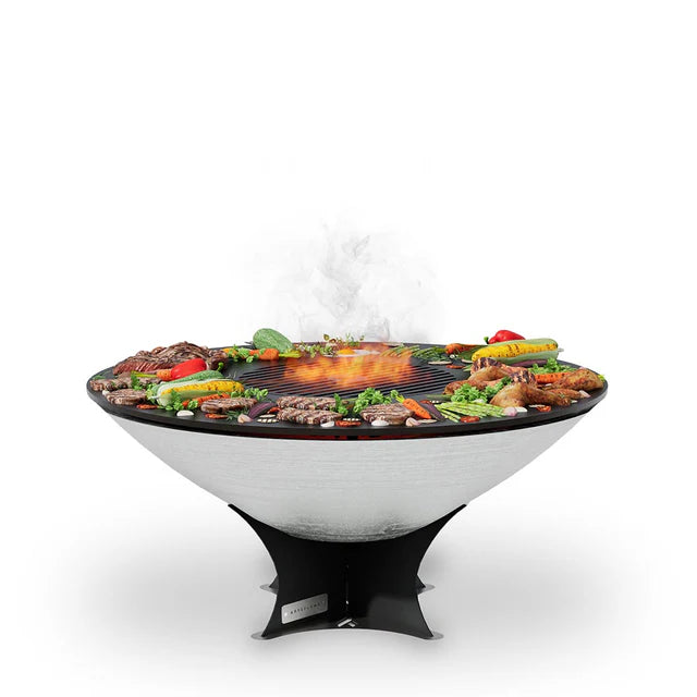 Arteflame 40" Platinum Series Fire Pit With Cooktop features a round cooking surface where you can arrange vegetables and meats around the perimeter, with flames centered in the middle The grill boasts a conical shape and is supported by a sleek black stand.