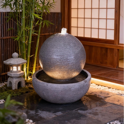 Luna Bowl water fountain with textured sphere and basin, illuminated in a modern Zen courtyard with bamboo and stone accents.