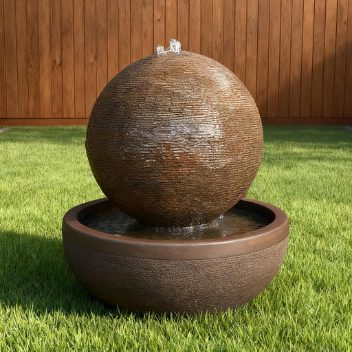 Luna Bowl water fountain with rustic textured sphere and wide basin, centered on a green backyard lawn near wood fence.