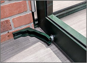 Green magnetic hinged door holder mounted on a stem wall, keeping the greenhouse door open at a 90-degree angle.