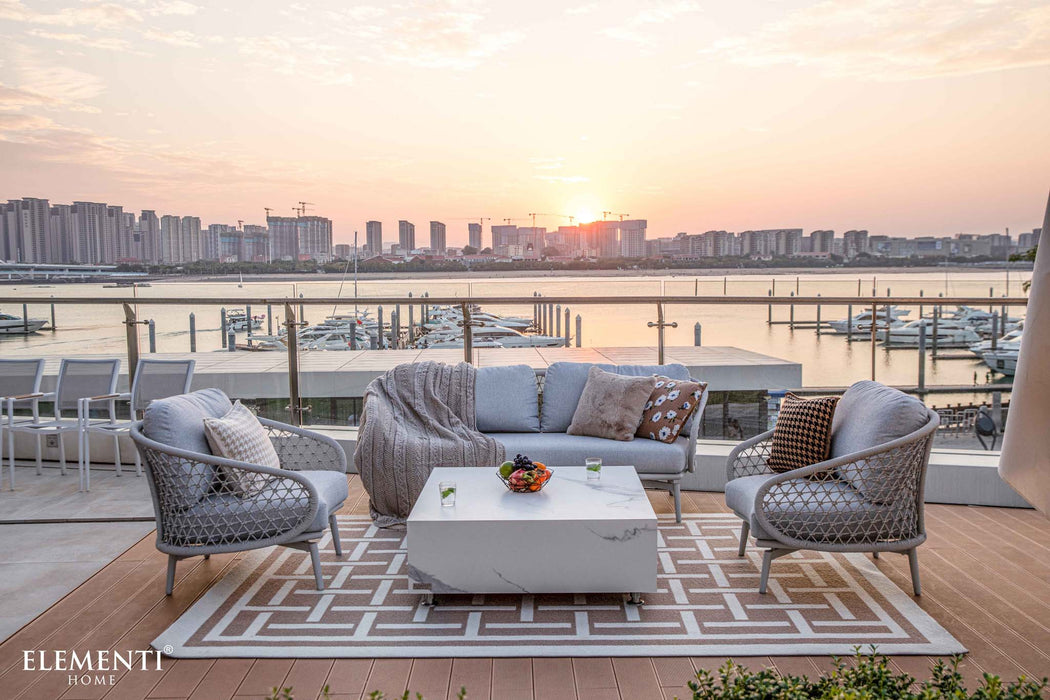 Outdoor lounge setting featuring the Elementi marble coffee table in Bianco White with sunset view and comfortable seating.