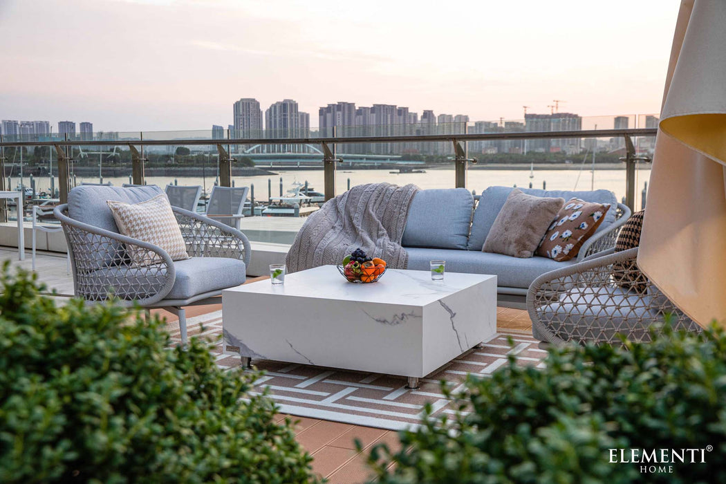 Marble square medium coffee table in Bianco White on an outdoor patio, styled with modern chairs and cityscape background.