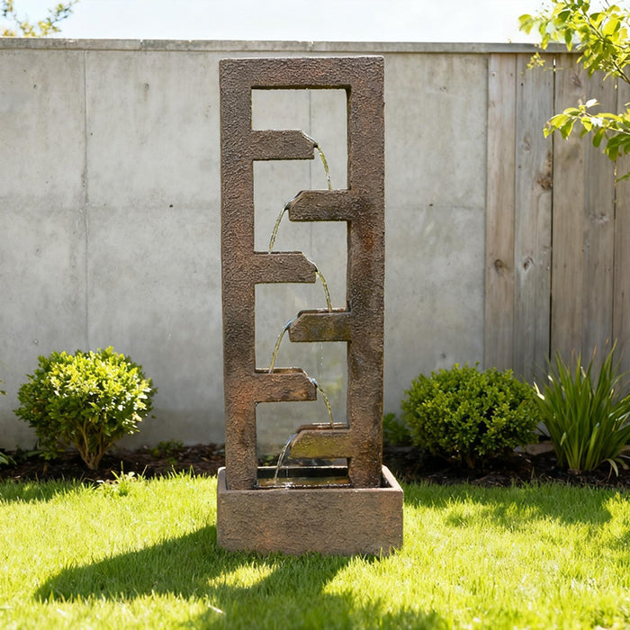 Minimalist cascade outdoor water fountain with four flowing tiers, styled in modern yard with concrete wall and shrubs
