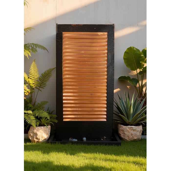 Minimalist copper panel wall fountain with black frame and base, styled with ornamental plants and smooth stones.