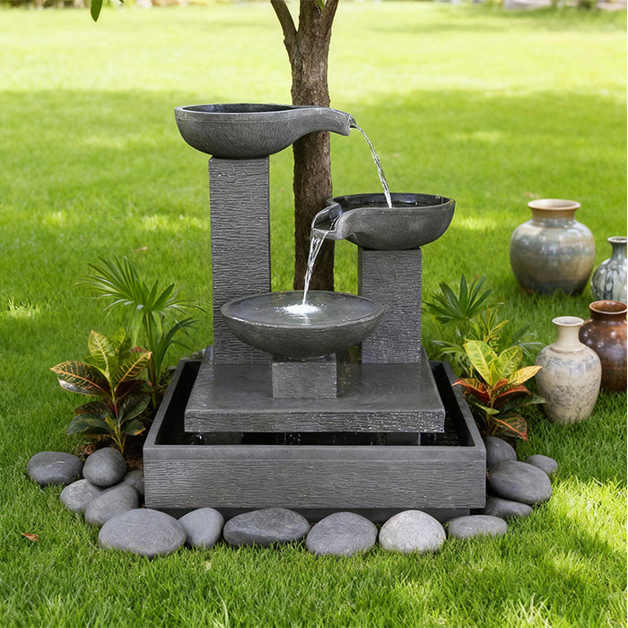 Modern Exaco Trio Bowl water fountain featuring three cascading basins on a square base surrounded by grass and decorative stones