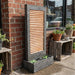 Modern outdoor wall fountain with horizontal copper panel and dark frame, placed against brick wall with planter base.