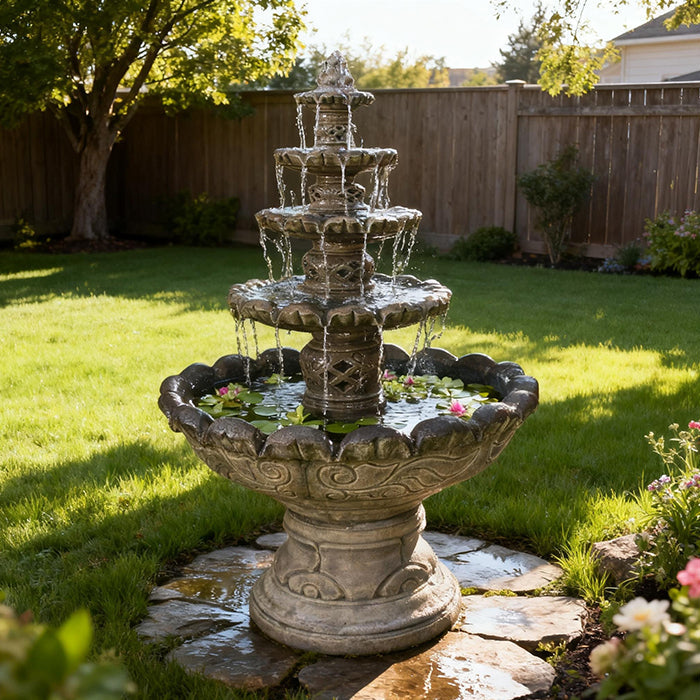 Monaco outdoor water fountain with four cascading tiers placed on a green backyard lawn with decorative stone base and flowers