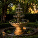 Monaco tiered outdoor garden water fountain in classic stone finish with cascading bowls and lily pads in a landscaped backyard