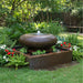 Contemporary moon bowl garden water fountain surrounded by colorful flowers and greenery in landscaped backyard setting.