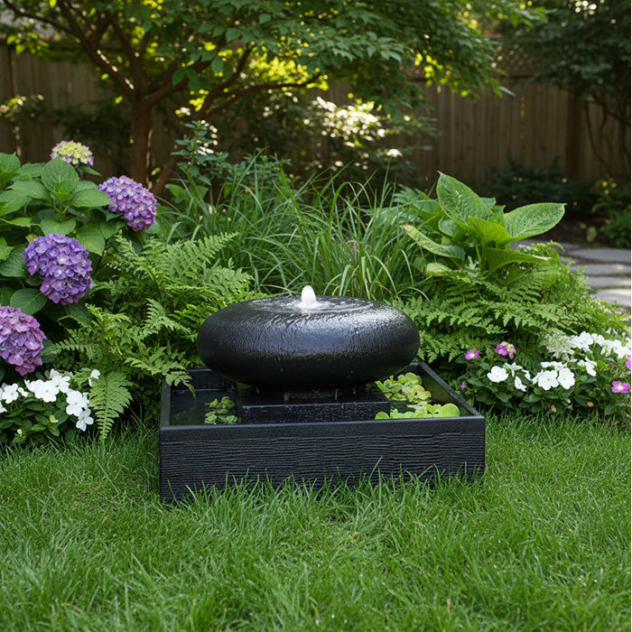 Elegant moon bowl water feature in square basin nestled in landscaped backyard with hydrangeas, ferns, and lush grass.