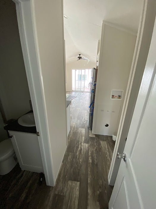 Narrow hallway leading to the kitchen in the Champion Home No Loft by Oasis Tiny Estates, with a view of the bathroom entrance.