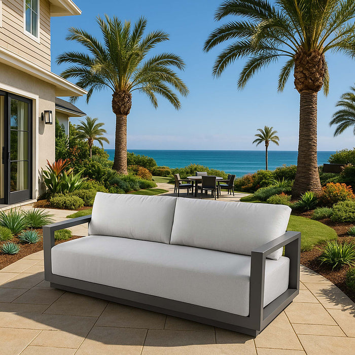 Newport Collection outdoor sofa by Elementi, set on a coastal patio with palm trees and an ocean view, ideal for relaxation.