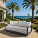 Newport Collection outdoor sofa by Elementi, set on a coastal patio with palm trees and an ocean view, ideal for relaxation.