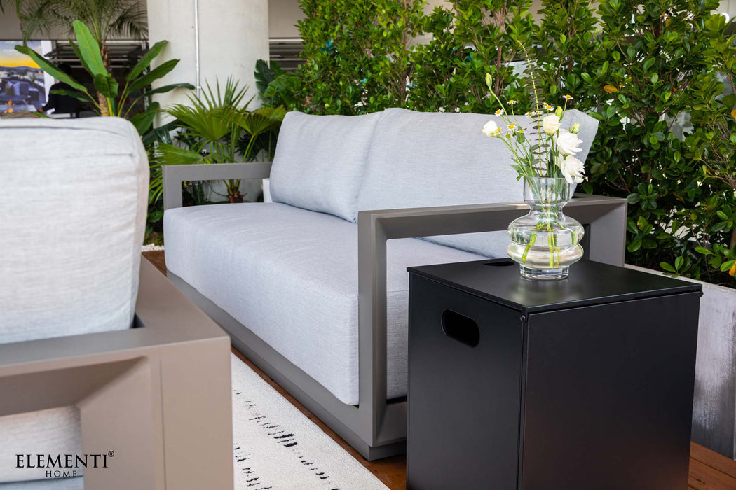 Close-up of the Newport Collection outdoor sofa and a black side table with a vase of flowers, part of Elementi's furniture.