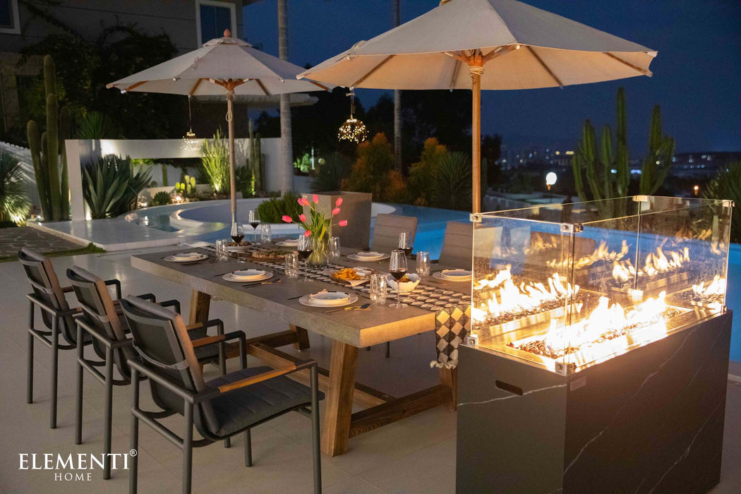 Elementi Seine Series rectangular dining table in a nighttime outdoor setting, with lit fire feature and cozy ambiance.