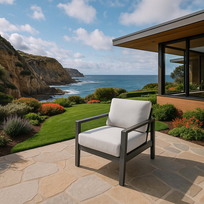 A comfortable lounge chair from the Elementi Outdoor Furnitures Laguna Collection on a stone patio with a scenic coastal backdrop.