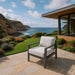 A comfortable lounge chair from the Elementi Outdoor Furnitures Laguna Collection on a stone patio with a scenic coastal backdrop.