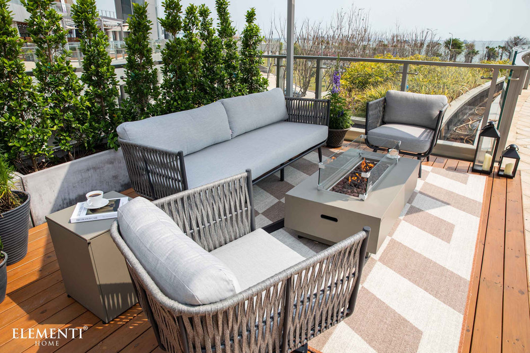 An inviting outdoor living space with Elementi Outdoor Furnitures Milano Collection seating, a fire pit, and a patterned rug on a wooden deck.