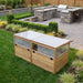 Greenhouse with Garden in a Box 6x3 on a manicured lawn, western red cedar frame with clear panel walls and hinged lids near a stone kitchen