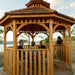Friends sharing wine inside the Outdoor Living Today 12' Bayside Panelized Octagon Gazebo, cedar shake roof and cupola above a lake view