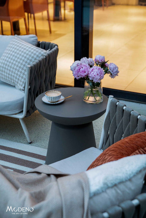 Slate black large side table from the Elementi Kylix Series, styled with flowers and a cup in an outdoor seating arrangement.