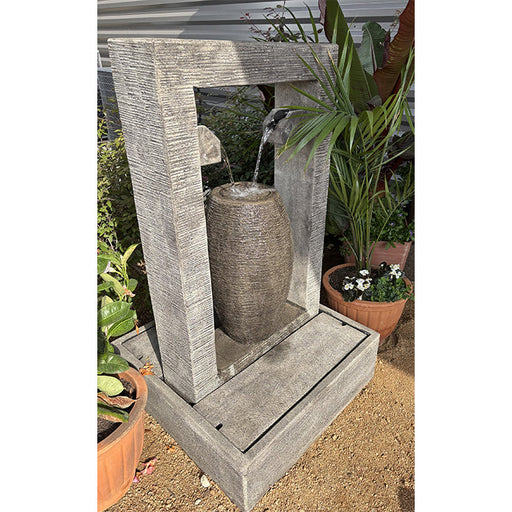 The Trevi Fountain displayed outdoors, featuring a light grey, textured concrete finish, with water cascading into its base, surrounded by green potted plants.