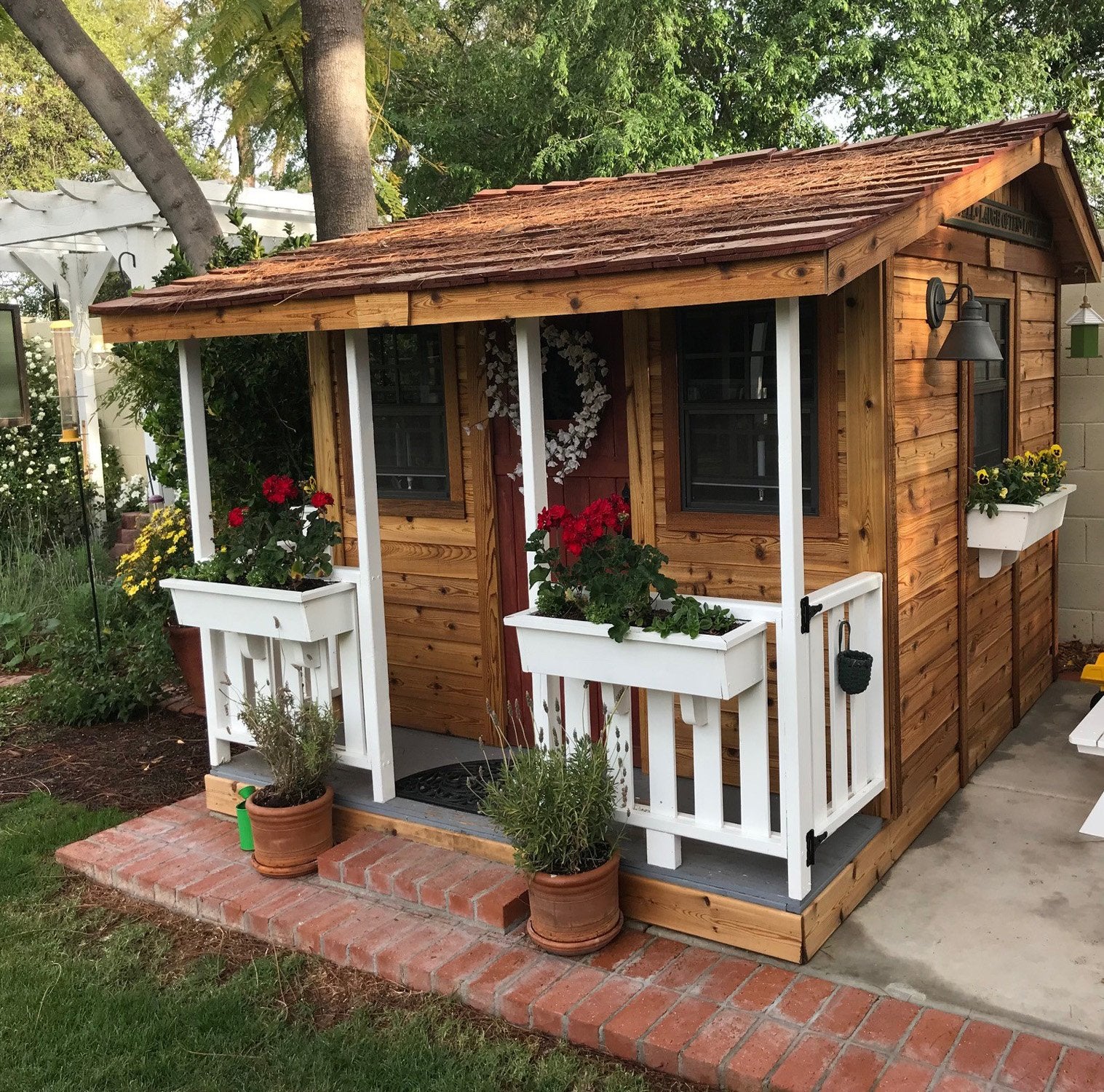 The Outdoor Living Today Cozy Cabin Playhouse with railings painted white. This small wooden playhouse adds charm to a backyard.