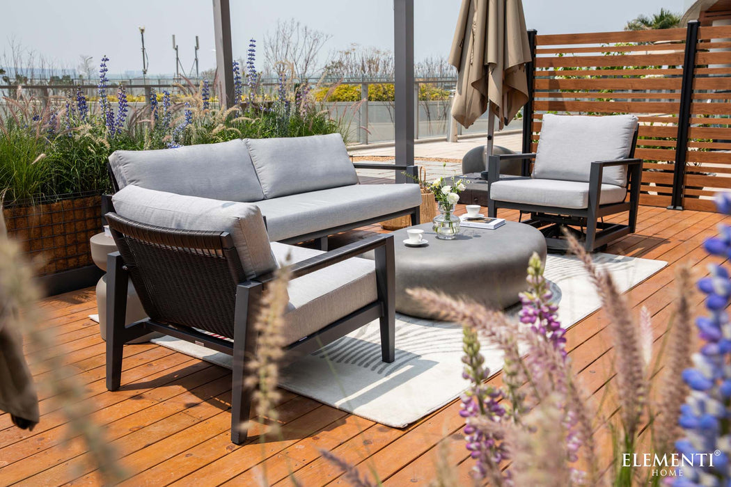 A complete patio lounge set from the Elementi Laguna Collection, featuring a sofa, chairs, and a round concrete coffee table on a wooden deck.