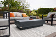 A cozy patio lounge featuring the Elementi Tevere Series Rectangle Large Coffee Table in Slate Black, styled with wine and snacks on a patterned rug.