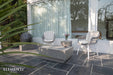 A cozy outdoor seating area featuring the Elementi Tevere Series Square Coffee Table in Space Grey alongside two lounge chairs on a stone patio.