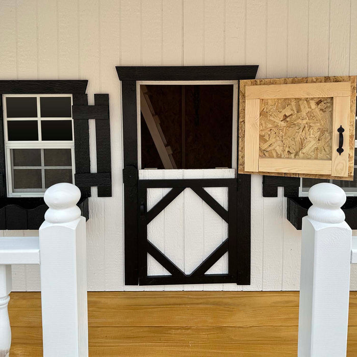 Front view of Little Cottage Co. Pennfield Cottage Playhouse featuring a black-and-white Dutch door, shuttered windows, and wooden porch railing detail.