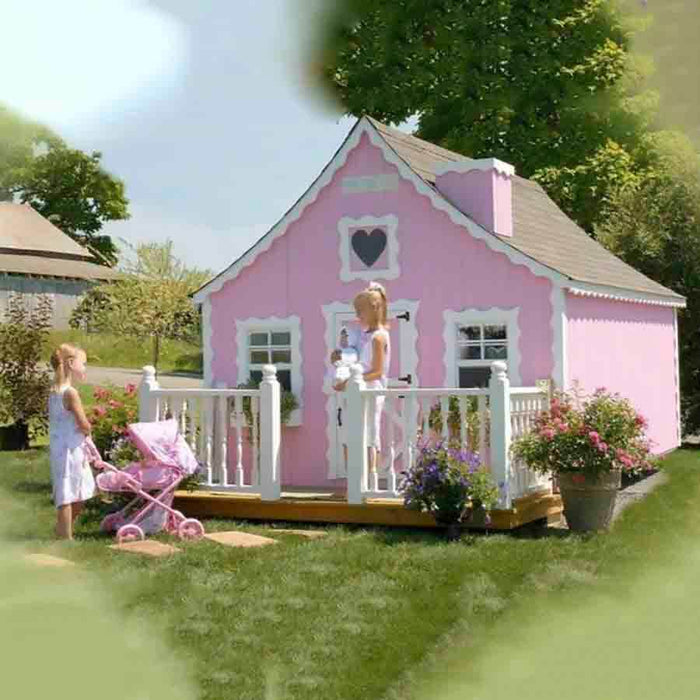 Scene of children playing on the front porch of the Little Cottage Company Gingerbread Cottage Playhouse, featuring white railings and pink accents.