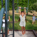 Girl hanging from the Lifetime playset's trapeze bar with gym rings while a boy climbs the ladder in the background.
