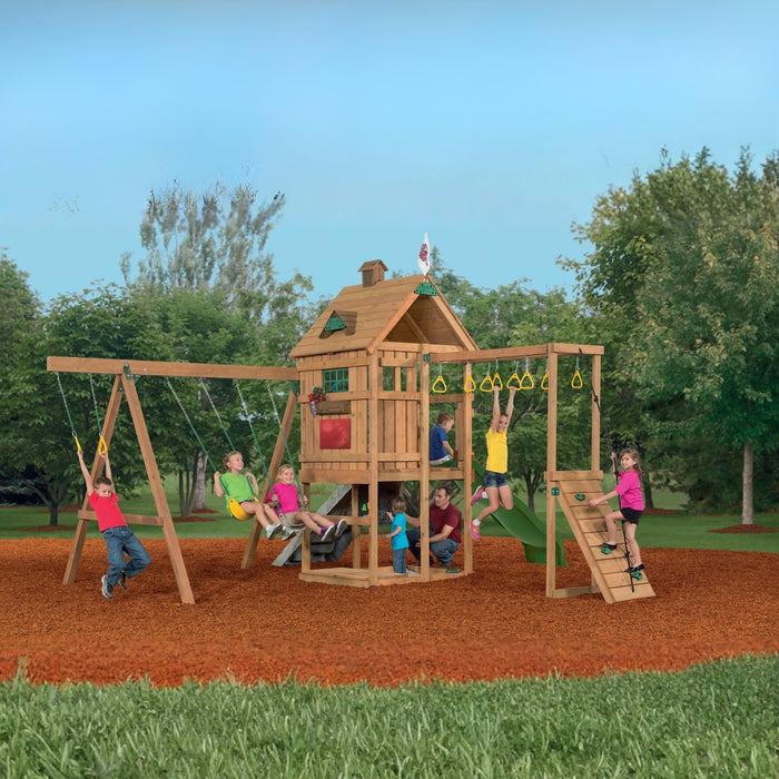 Children playing on the Playstar Contender Silver playset, featuring yellow slide, swings, monkey bars, and wooden clubhouse in a backyard setting.