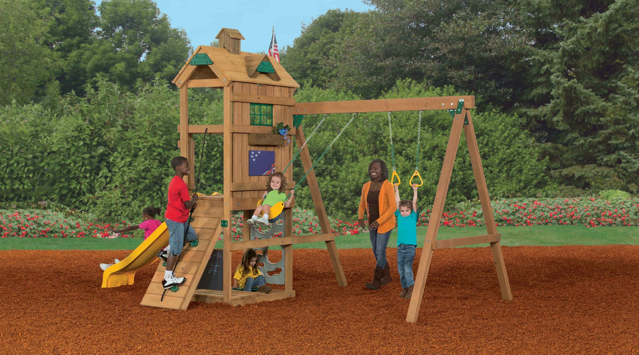 Children playing on Playstar Trainer Bronze playset with swings, climbing wall, and slide outdoors