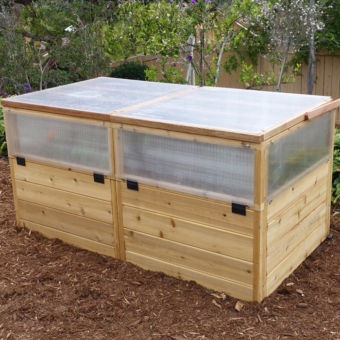 Three-quarter view of the 6x3 cedar Greenhouse with Garden in a Box, clear panel sides and hinged lids closed over the raised planting bed