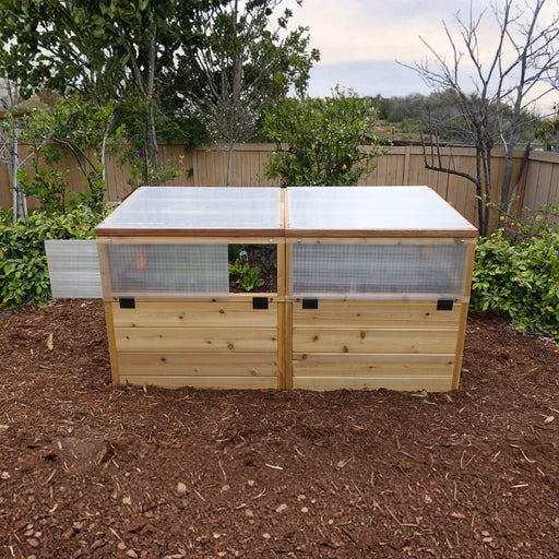 Front view of the RB63 Greenhouse with Garden in a Box, cedar raised bed with twin polycarbonate roof panels on bark mulch by a citrus grove