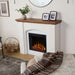 Real Flame Anika white electric fireplace mantel styled in cozy living room with wood mantel, faux tile surround, glowing flames, plant, framed photos, and log basket beside it