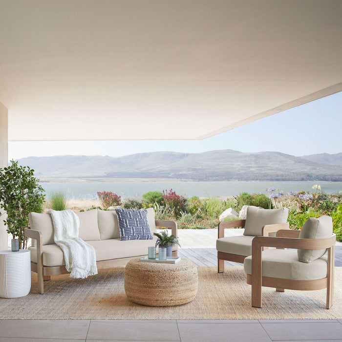 The Real Flame Arlo Outdoor Seat Sofa with Cushions set arranged on a patio overlooking a lake and mountains, styled with a woven ottoman and greenery.