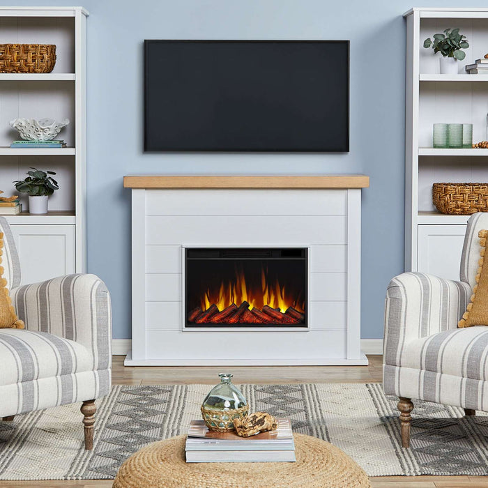 Real Flame Marshall Slim Electric Fireplace in white styled in living room with TV mounted above, flanked by built-in white bookshelves and striped accent chairs