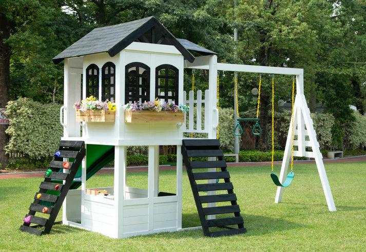 a product image of the 2MamaBees Reign Two Story Playhouse on a garden space with trees in the background