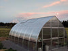 Riga XL 6 Greenhouse by Exaco Hoklartherm set against mountain backdrop at sunset, showcasing its sturdy polycarbonate frame for all-season growing.