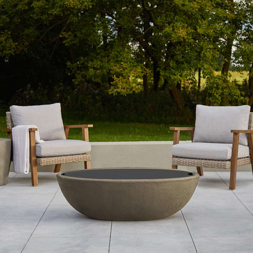 Outdoor patio setup featuring a fire bowl covered with the Riverside Oval Burner Lid by Real Flame, surrounded by two armchairs