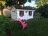 Riverside storage shed with all accessories painted white in the backyard in front of pink lawn chairs