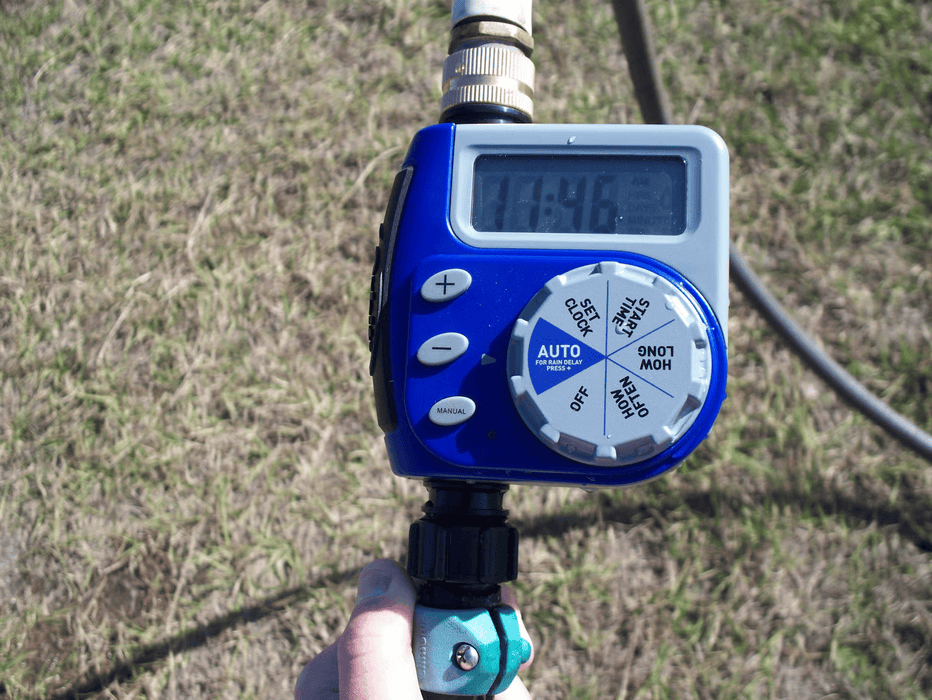 Close-up of Riverstone Greenhouse Internal Watering System control timer with digital display and hose connection outdoors.